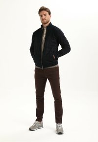 Marine ritsjack met een gestructureerde, gevoerde bovenkant, beige gebreide kraag, brown broek en grijze sneakers met witte zolen en veters.
