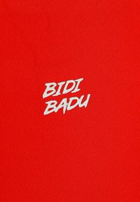 Tela roja con textura de canalé que presenta las palabras "BIDI BADU" en letras blancas, en negrita y ligeramente inclinadas, colocadas de manera destacada.