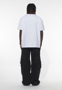 White cotton t-shirt with a relaxed fit, short sleeves, and rounded neckline, paired with black cargo pants featuring side pockets.