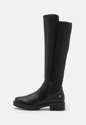 Botas negras hasta la rodilla hechas de cuero suave con acentos texturizados, un tacón bajo y un diseño de punta redondeada. Presentan un detalle de logo cerca del tacón.