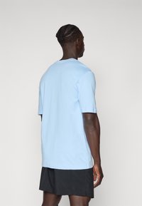 T-shirt de algodão azul claro com mangas curtas e decote redondo, visto de trás. O tecido parece suave e leve.