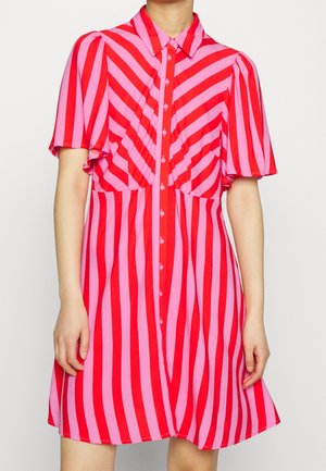 Robe à manches courtes avec des rayures diagonales et verticales rouges et roses, boutonnée devant, avec un col pointu, portée par une personne.