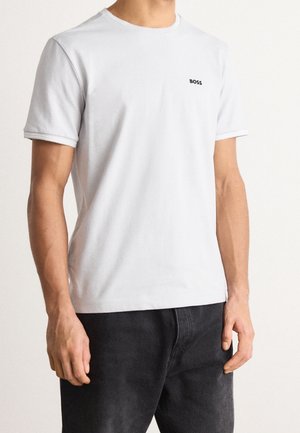 Jasnoszara koszulka z krótkim rękawem wykonana z bawełny, z okrągłym dekoltem i małym czarnym logo na lewej klatce piersiowej.