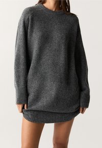 Maglione oversize grigio con polsini e bordo a coste. Tessuto morbido, scollo rotondo e design con retro più lungo. Stile minimalista.