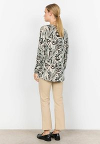 Chemise à manches longues, à motifs dans des couleurs claires avec des formes abstraites, associée à un pantalon beige et des chaussures noires, vue de dos.