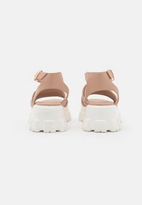 Nude sandals with adjustable ankle strap, featuring a white chunky sole for grip and a textured heel for enhanced stability.