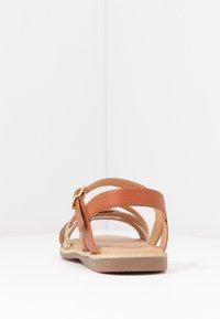 Brązowe sandały na płaskim obcasie z paskami, z górną częścią wykonaną z ekologicznej skóry, płaską podeszwą, złotym zapięciem i subtelnym metalicznym wykończeniem wzdłuż krawędzi.