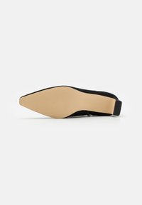 Zapato negro de punta con textura de ante. Cuenta con un tacón bajo negro y una suela lisa color tostado con líneas de tracción.