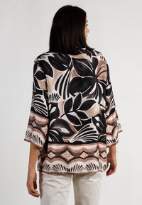 Bluse mit floralem Muster in Schwarz- und Beigetönen, aus leichtem Stoff, mit 3/4-Ärmeln und dekorativem Saum am unteren Rand.