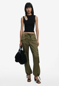 Zwarte mouwloze top met een uitsnijdetail; olijfgroene wijde broek met cargozakken en een trekkoord; geaccessoireerd met een zwarte tas.