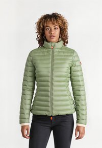 Groene pufferjack met hoge kraag, horizontaal gestikt patroon, rits aan de voorkant en een oranje ritslip. Zachte, gladde textuur.
