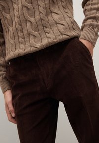 Suéter beige de punto grueso y pantalones de pana marrón oscuro con textura acanalada; los pantalones tienen bolsillos laterales y un ajuste relajado.