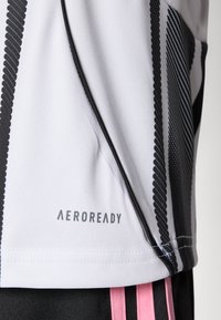 T-shirt de sport à manches courtes en gris clair avec des rayures verticales noires, arborant le logo "AEROREADY", texture lisse et design discret.