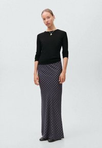 Dlouhá kostkovaná sukně v námořnické modři a fialové s úzkým střihem, zkombinovaná s přiléhavým černým topem s dlouhým rukávem. Hladká textura, ležérní design.