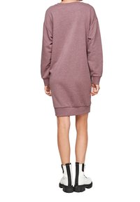 Ylipitkä, pitkähihainen mekko pölyruusun värisestä fleece-materiaalista, jossa ribbireunat hihansuissa ja helmassa, yhdistettynä paksuihin valkoisiin saappaisiin, joissa on mustia yksityiskohtia.