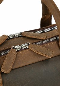 Bolso de cuero marrón con dos cremalleras plateadas y tiradores de cremallera marrones. Textura desgastada con costuras en contraste y asas resistentes.