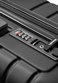 Valigia rigida nera con superficie testurizzata, un lucchetto combinato con tre dischi e un meccanismo di chiusura con marchio.