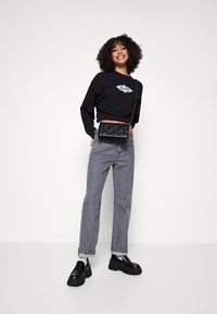 Felpa nera corta con stampa grafica, jeans dritti grigi, borsa a tracolla nera trapuntata e scarpe piattaforma nere spesse.