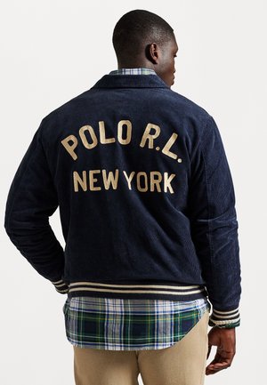 Navy corduroy jacket features "POLO R.L." and "NEW YORK" in gold lettering, with striped ribbed cuffs and a plaid shirt underneath.