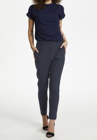 Marineblauw T-shirt met korte mouwen, gecombineerd met op maat gemaakte donkergekleurde broek met zakken en een slim-fit ontwerp. Gemaakt met zwarte hoge hakken.