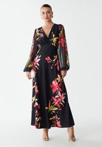 Abito lungo nero con stampa floreale in rosa e giallo. Presenta maniche lunghe in trasparenza e scollatura a V. Tessuto liscio, design fino a terra.