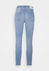 Jean slim bleu clair avec deux poches arrière et une étiquette à la taille, présenté de dos sur fond blanc uni.