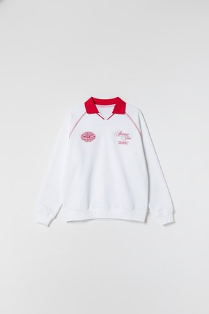 Fehér pulóver piros gallérral, elején rózsaszín hímzett logókkal és felirattal. Hosszú ujjú, bordázott mandzsettákkal és szegéllyel.