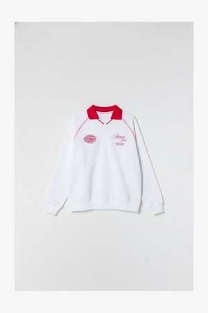 Fehér pulóver piros gallérral, elején rózsaszín hímzett logókkal és felirattal. Hosszú ujjú, bordázott mandzsettákkal és szegéllyel.