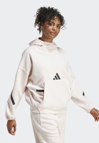 Light pink sweatshirt with a high collar, oversized fit, and front pocket. Features black stripes on the sleeves and logo on the chest.