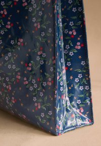 Cvetna torba z mornarsko modro podlago, večbarvnimi cvetovi in listi, s sijočo površino in strukturirano obliko.