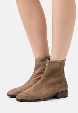 Bottines en daim marron avec un talon bloc, présentant un design épuré et élancé, ainsi qu'une fermeture éclair sur le côté intérieur. Texture lisse.