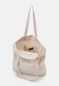 Sac cabas beige en velours côtelé avec deux longues anses, coutures renforcées, poche intérieure et motif côtelé texturé. Ouverture supérieure, design spacieux.