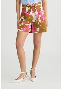 Pantaloni corti con motivo floreale in marrone, rosa e bianco, con vita alta e lacci. Abbinati a scarpe bianche con punta e cinturini alla caviglia. Design minimalista.