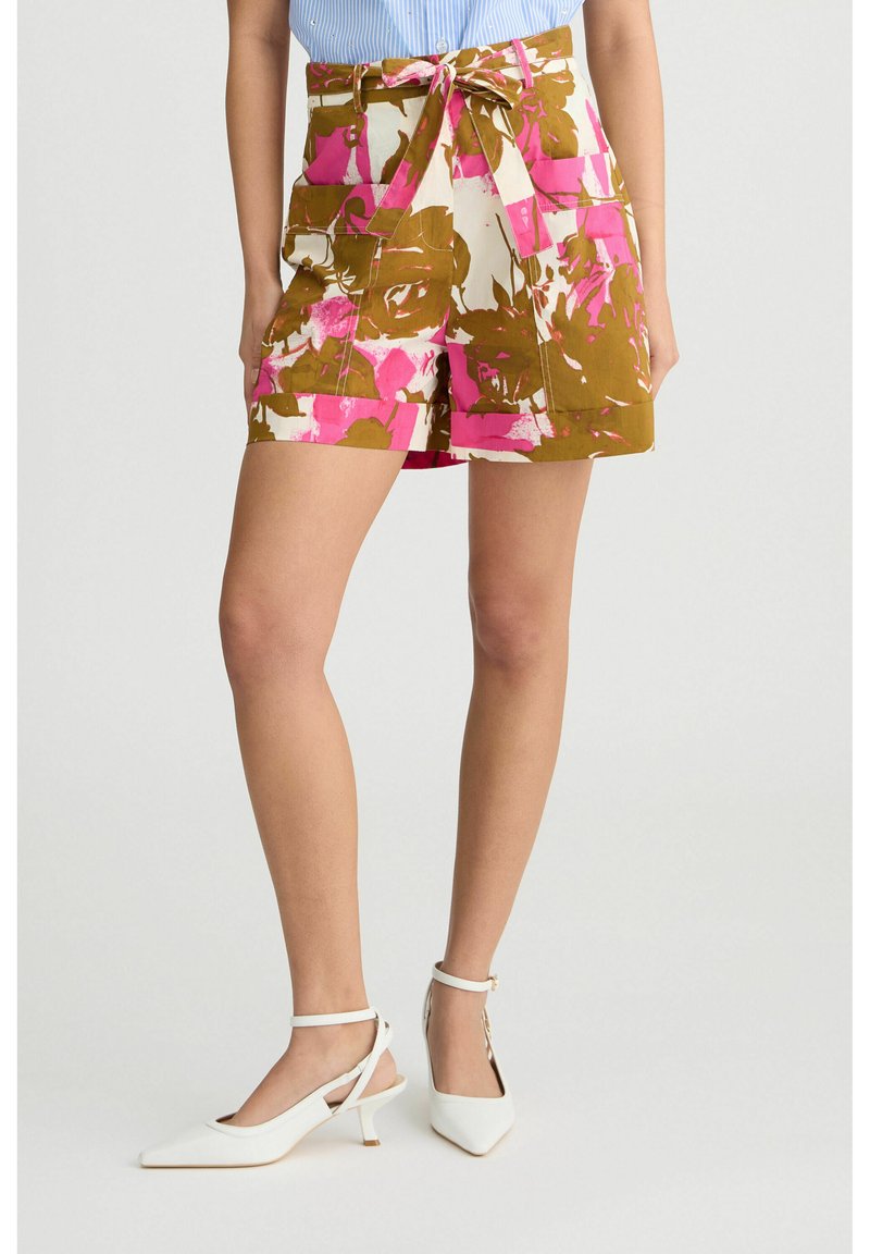 Pantaloni corti con motivo floreale in marrone, rosa e bianco, con vita alta e lacci. Abbinati a scarpe bianche con punta e cinturini alla caviglia. Design minimalista.