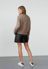 Hnedý pletený sveter s okrúhlym výstrihom, v kombinácii s čiernymi koženými šortkami. Biele tenisky s olivovými akcentmi dopĺňajú outfit.