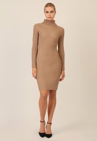 Strikket turtleneck kjole i beige med ribbet tekstur, tætsiddende silhuet, lange ærmer og over-knee længde, parret med sorte hæle.