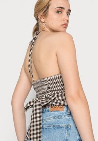 Top halter em padrão vichy castanho e branco com laço nas costas, combinado com calções de ganga de cintura alta em azul claro com uma etiqueta de couro.