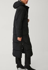 Zwarte pufferjas met een capuchon, met een lange, gevoerde ontwerp, drukknoopsluiting en zijzakken; gladde, glanzende textuur.