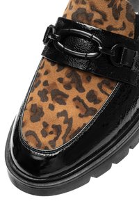 Obermaterial aus braunem Wildleder mit Leopardenmuster, kontrastiert durch einen glänzenden schwarzen Lacklederbesatz und einen Riemen mit schwarzem Beschlag. Dicke schwarze Sohle.