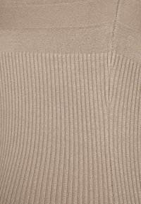 Beige ribbet strikket stoff med en glatt tekstur, med vertikale striper og en sømdetalj. Materialet ser ut til å være strekkbart og fleksibelt.