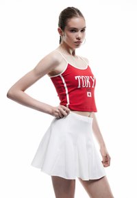 Czerwony bawełniany crop top z białym wykończeniem i nadrukiem "TOKYO JAPAN", zestawiony z białą plisowaną mini spódnicą. Gładka tekstura, dopasowany fason.