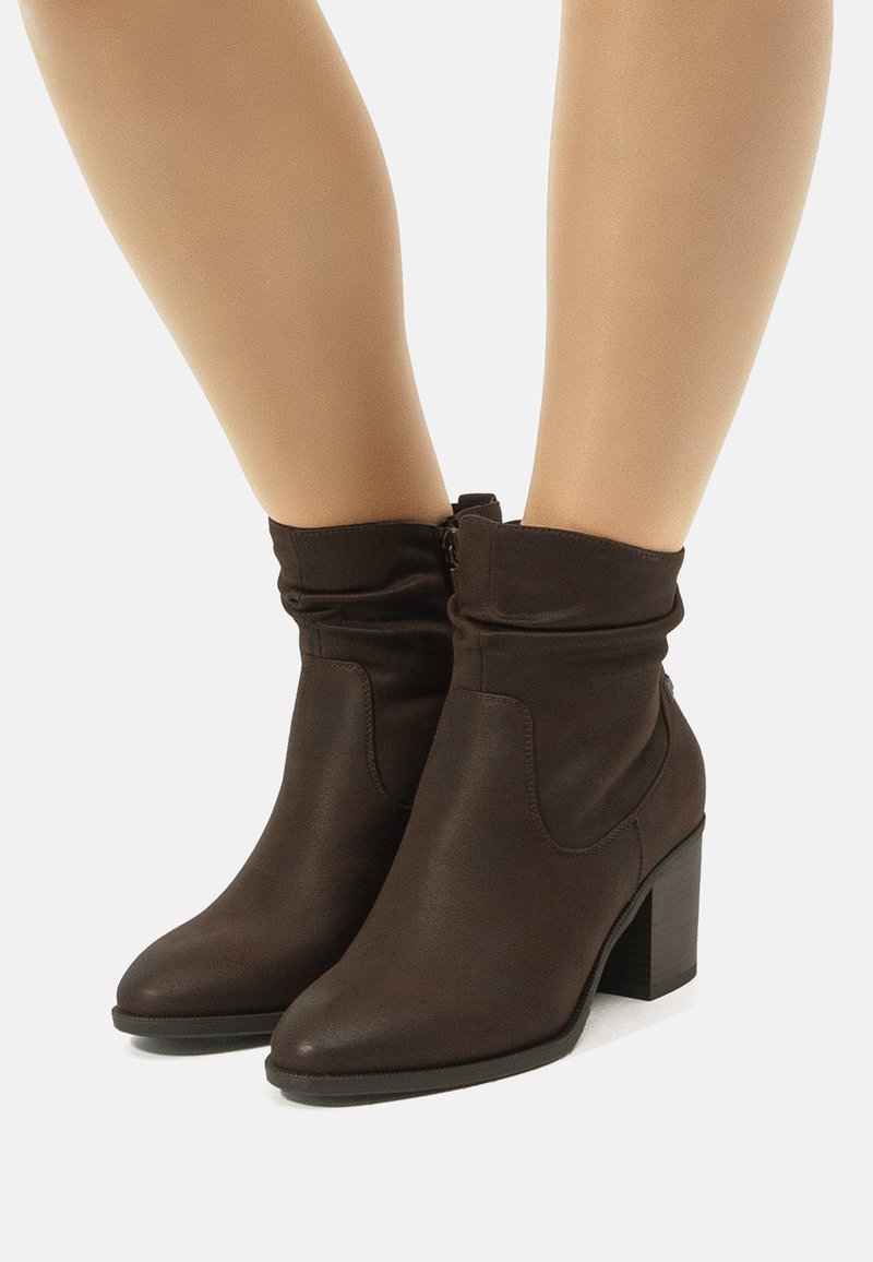 Botas tobilleras marrones con un diseño arrugado, material de imitación de cuero suave, punta afilada y tacón cuadrado cónico. Detalle de cremallera en la parte posterior.