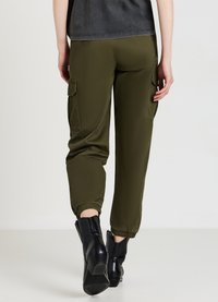 Olivgrüne Cargo-Hosen mit elastischen Bündchen, Seitentaschen und entspannter Passform, kombiniert mit schwarzen Knöchelschuhen.