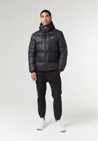 Črno odejana jakna s kapuco, z zadrgo in stranskimi žepi. Oblečena s črnimi hlačami cargo in belimi supergami.