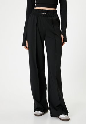 Zwarte wijde broek met een smockband in de taille en het "REPEAT" logo. Gemaakt van zacht materiaal met een gladde textuur en minimale naden.