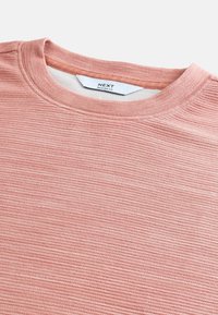 Camiseta de corte relajado en color rosa claro, con una tela estriada texturada, escote redondo y una etiqueta que dice "NEXT" en el cuello interior.