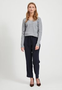 Pilkas v-neck megztinis, pagamintas iš minkštos tekstilės, derinamas su tamsiai mėlynomis kelnėmis su raišteliais. Modelis vilki leopardų rašto aukštakulnius batelius, o plaukai ilgi, banguoti, leisgyviais.