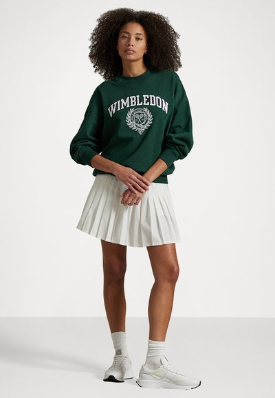 Grønn hettegenser med "Wimbledon" tekst og logo-design. Kombinert med en plissert hvit skjørt og hvite sneakers.