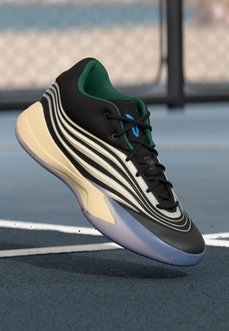 Chaussure de sport en noir et blanc avec intérieur vert et semelle bleue, flottant au-dessus d'un terrain de sport bleu près des lignes blanches du terrain.