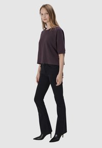 Fioletowa krótka koszulka z krótkimi rękawami, w połączeniu z czarnymi dzwonami. Modelka ma na sobie czarne szpilki. Prosty design, jednolite kolory.